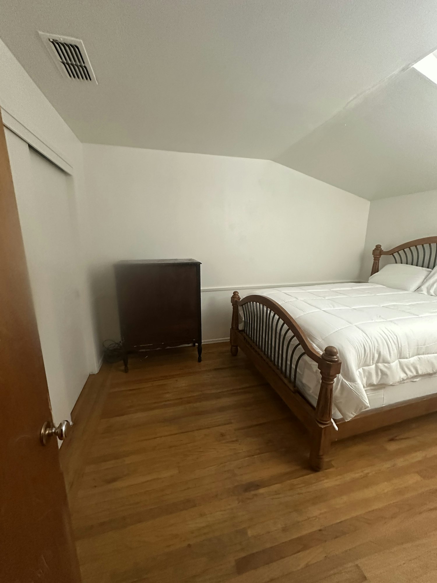 A room with a wooden bed, mattress, wooden floor, white walls, and a small dresser.