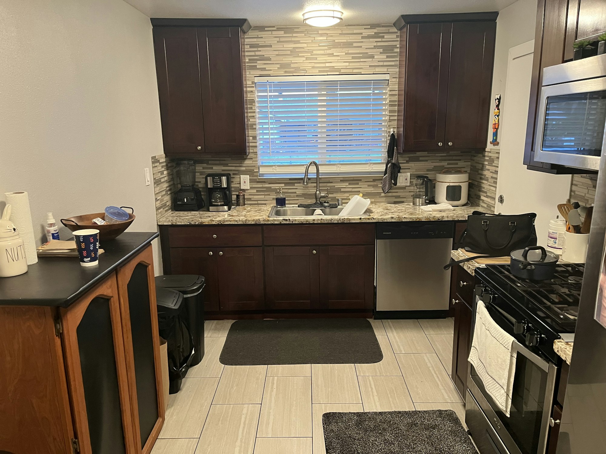 A modern kitchen with dark cabinets, granite countertops, appliances, and a small dining area. Clean and well-organized.