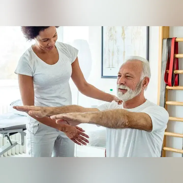 A therapist assists an elderly man with exercises in a bright, soothing therapy room.