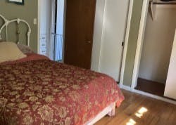 A bedroom with a red patterned bedspread, an open closet, and a closed wooden door.