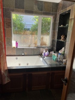A bathroom with a jacuzzi tub, window, and shelves holding various toiletries and decorations.