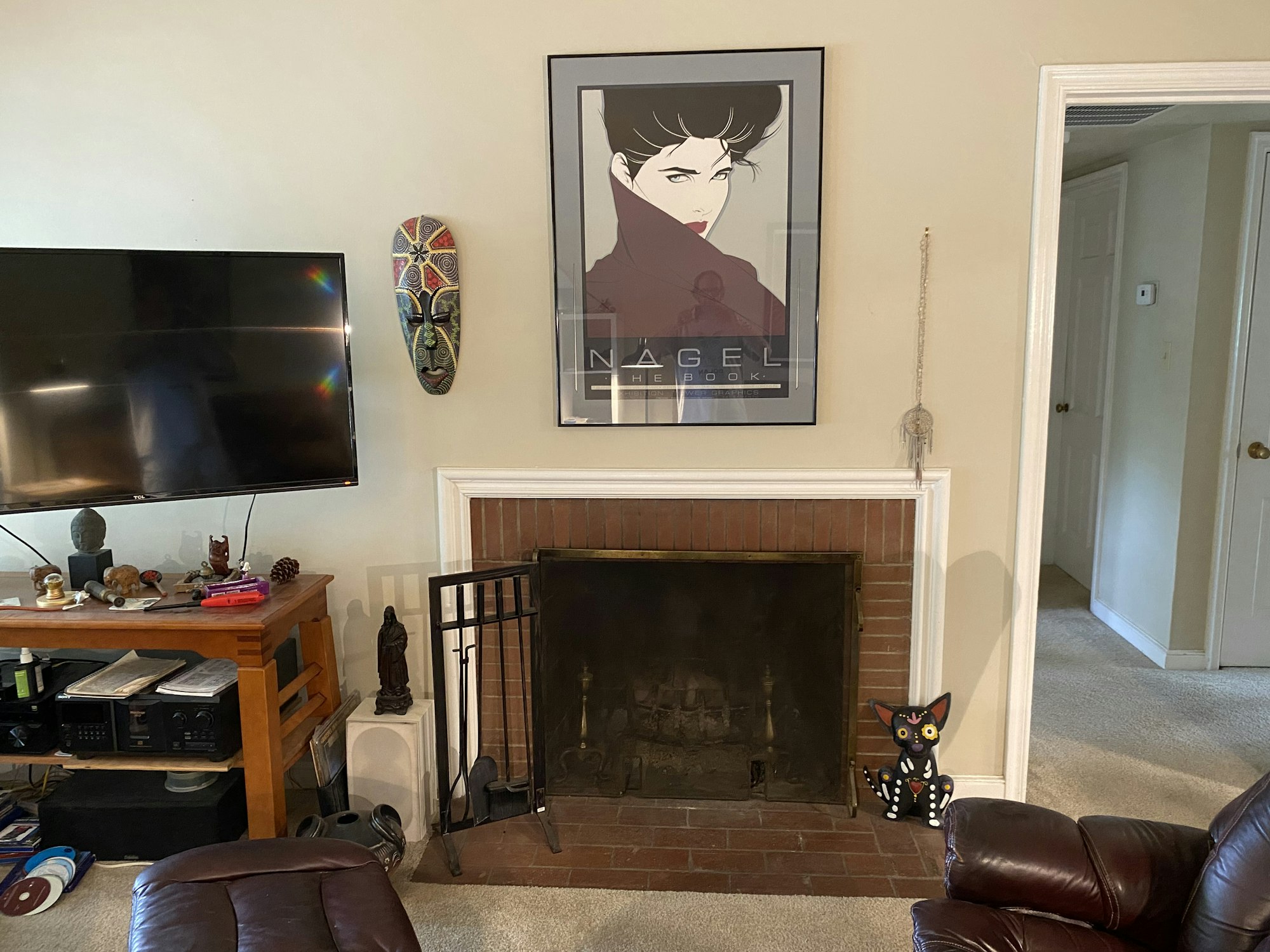 A living room with a TV, a framed poster, a fireplace, African mask, small statues, and a decorative cat figure.