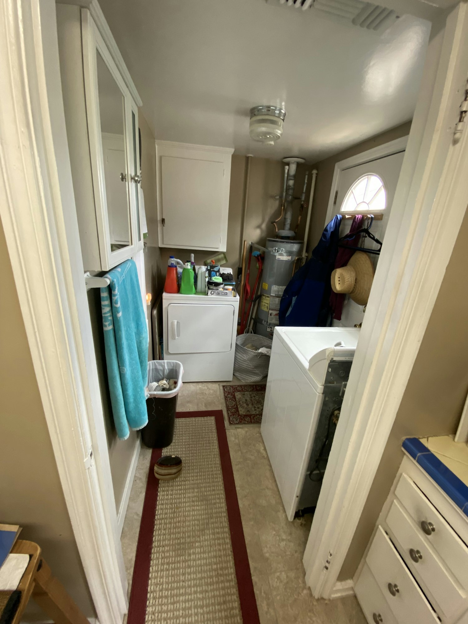 Laundry room with washer, dryer, water heater, cleaning supplies, and a trash can.