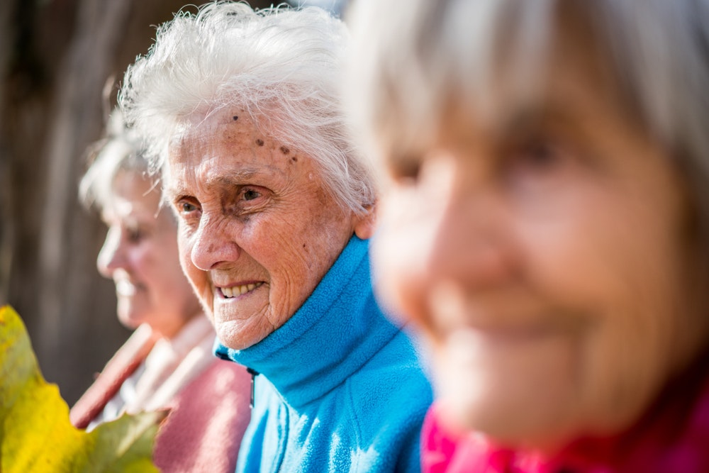 Elderly women with joyful expressions, focus on the woman in the foreground wearing a blue scarf.