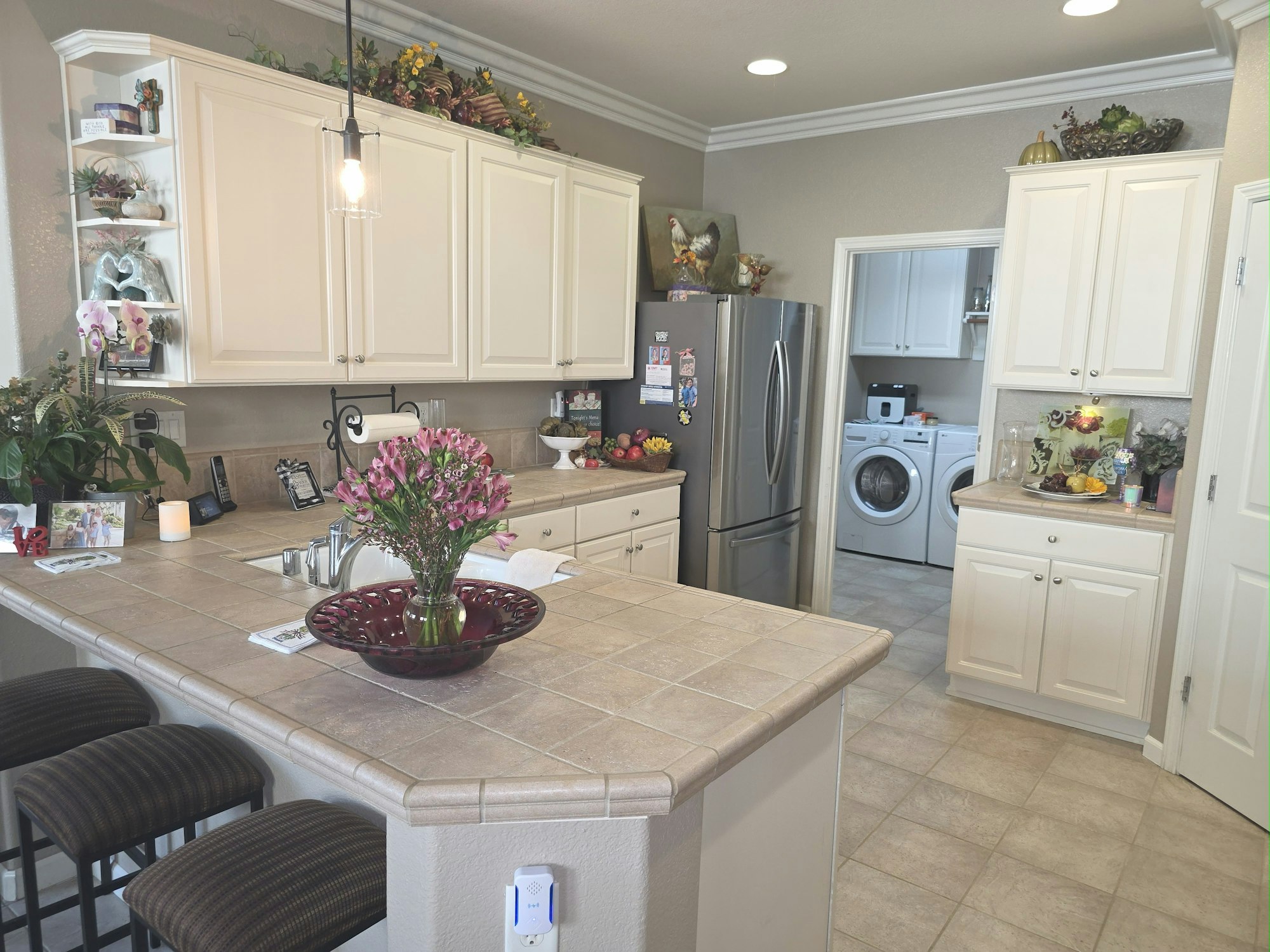A kitchen with white cabinets, center table with flowers, a fridge, and a view into a laundry room with a washer and dryer.