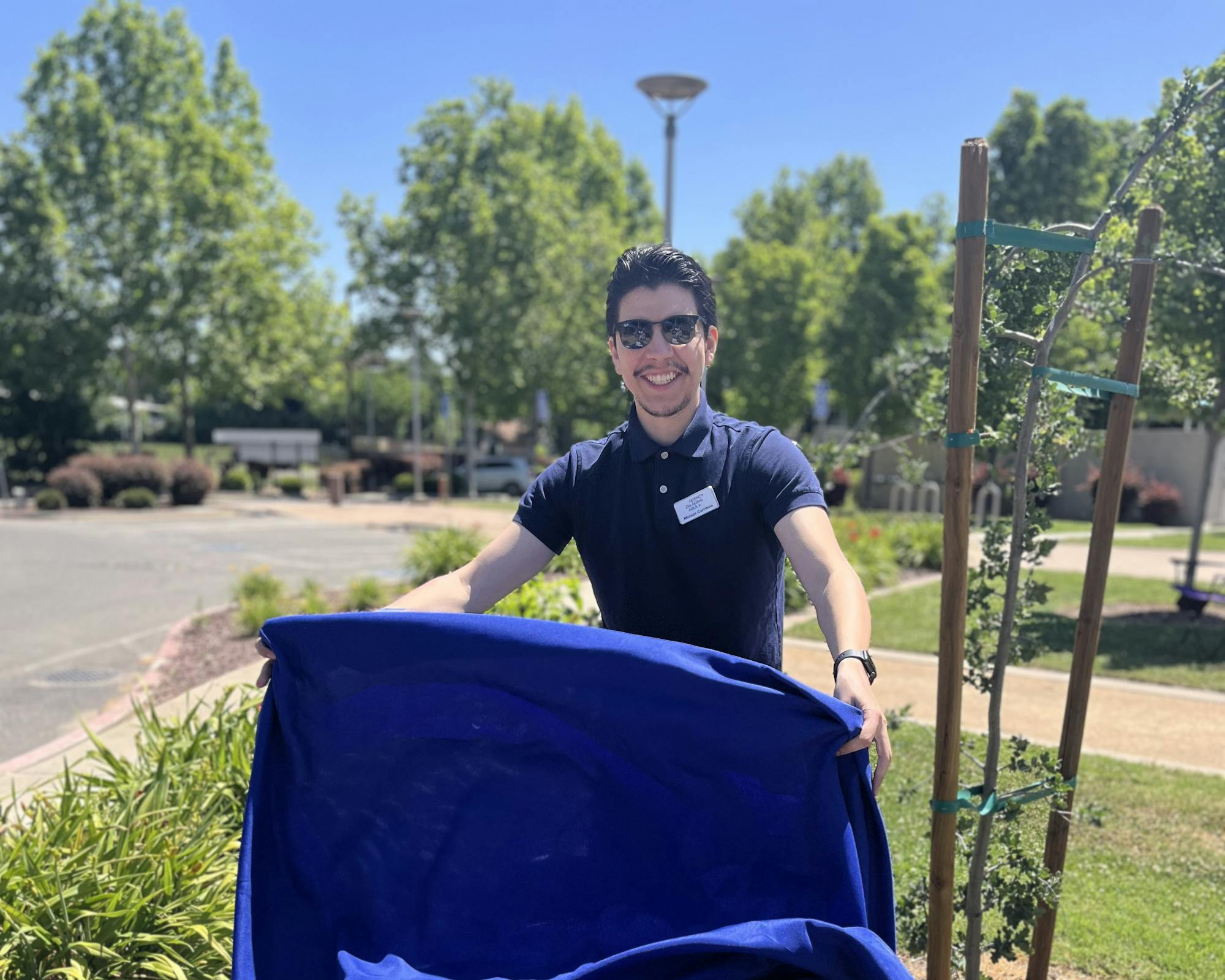 A smiling person behind a blue draped chair outside on a sunny day.