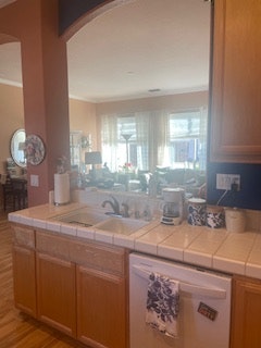 A kitchen with wooden cabinets, a tiled countertop, and various kitchen appliances on display, bathed in natural light.