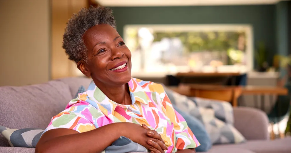 A smiling woman sitting comfortably on a couch with a colorful top.