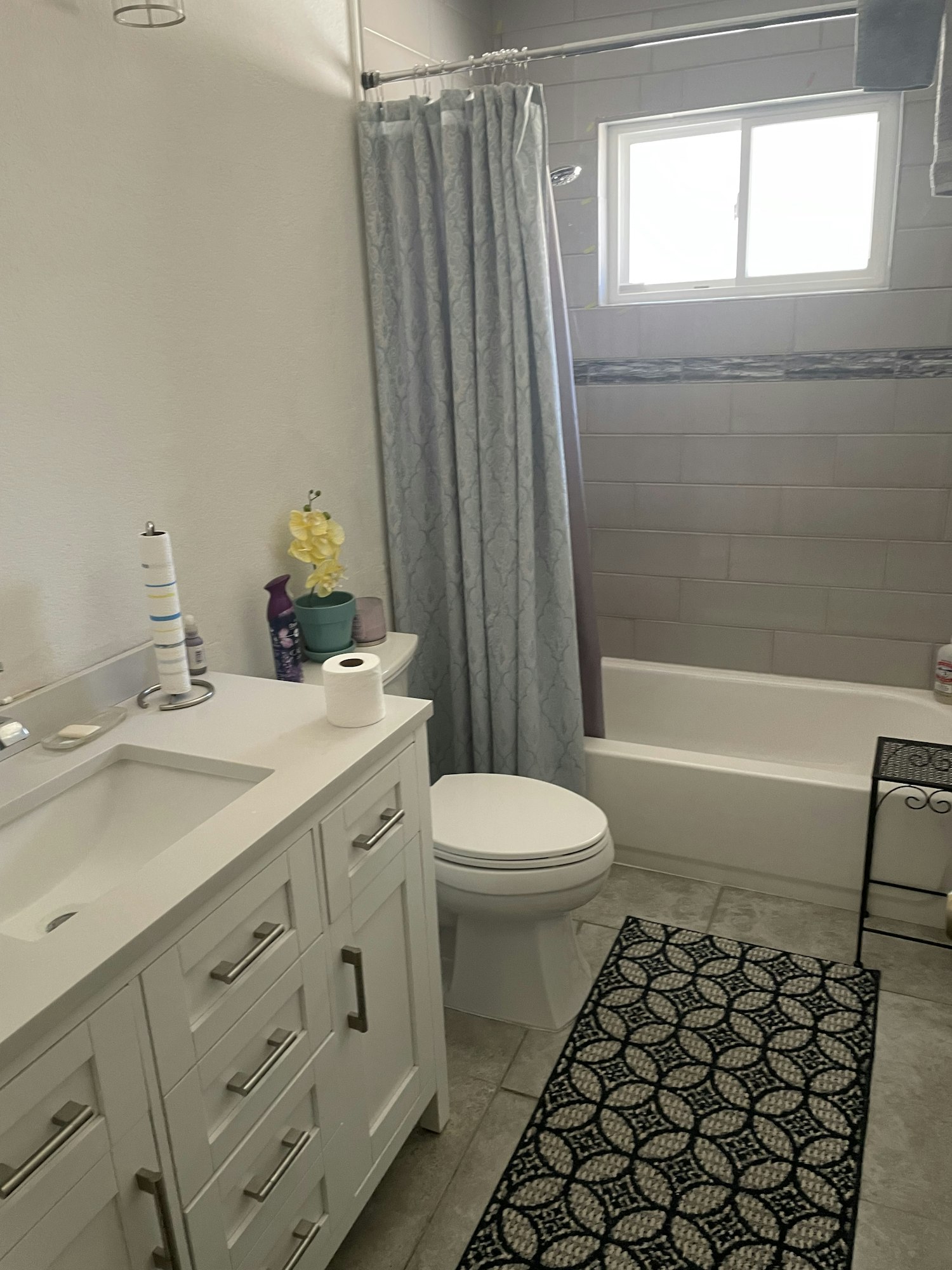 Bathroom with a sink, vanity, toilet, shower curtain, window, and patterned rug.