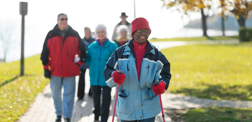 Group of smiling people engaging in outdoor walking exercise, with a focus on a person in the front.