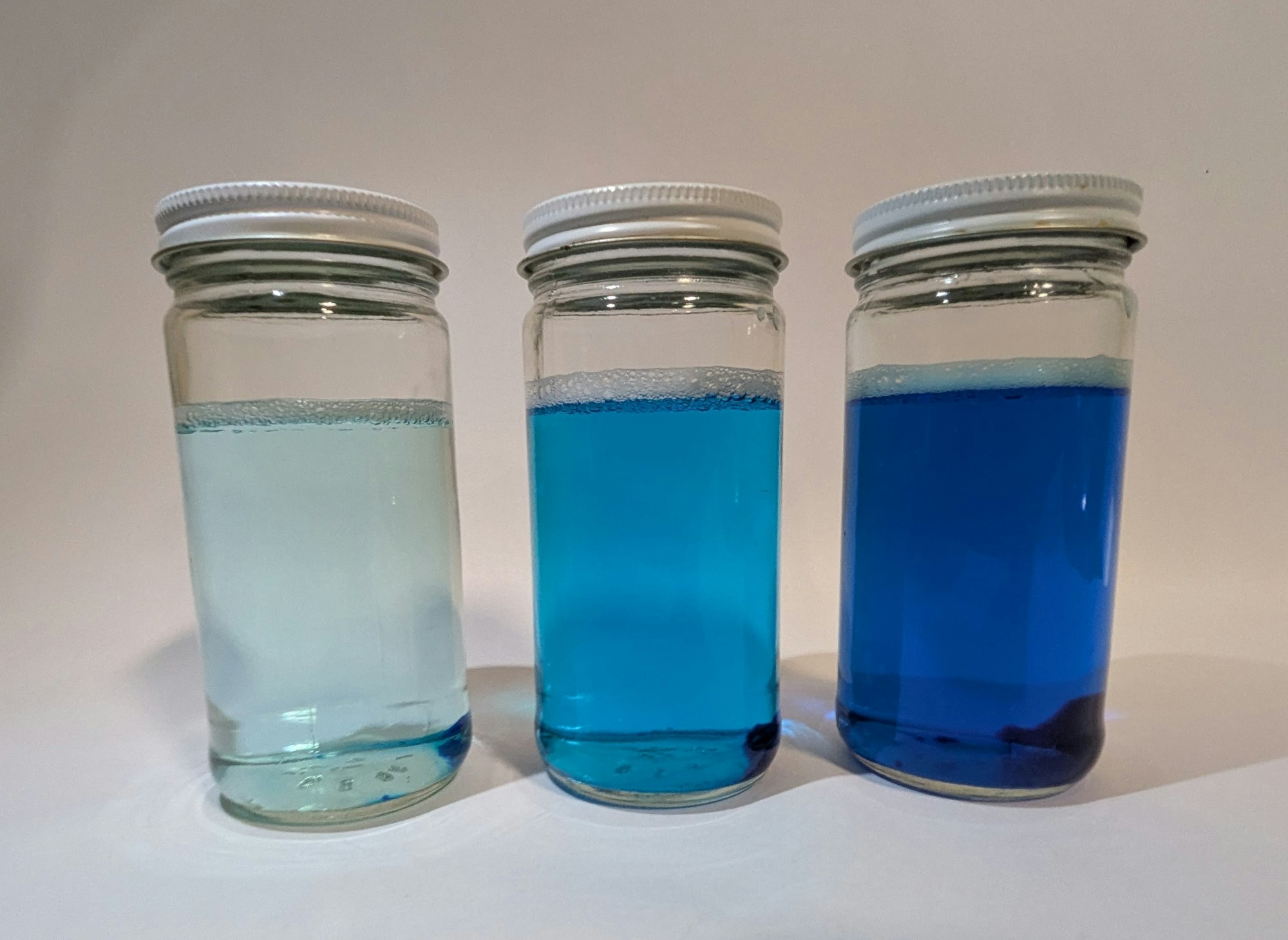 Three jars with white lids filled with liquids in varying blue shades.