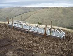 Cattle water trough with structure over it on a hillside with a view of rolling hills in the background.