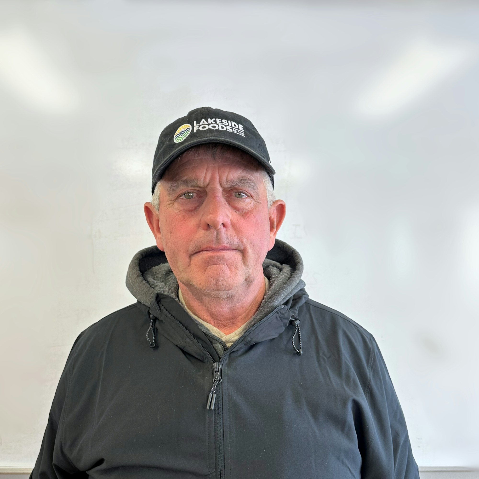 A man wearing a black "Lakeside Foods" cap and a jacket stands in front of a white background.