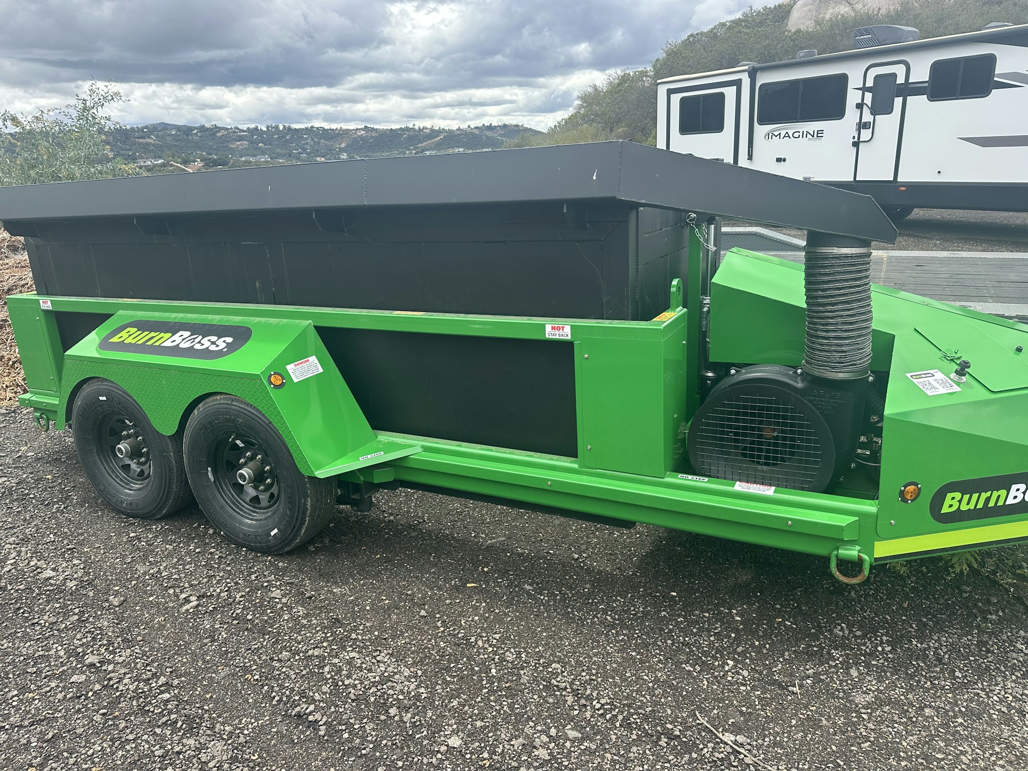 The image shows a green trailer designed for burning waste, labeled "Burn Boss." It's parked on a gravel surface.