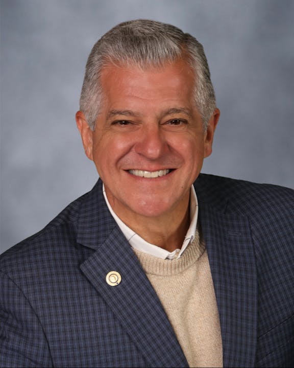 Portrait of Board Member Dino Pick Smiling in Gray Suit Jacket with neutral background