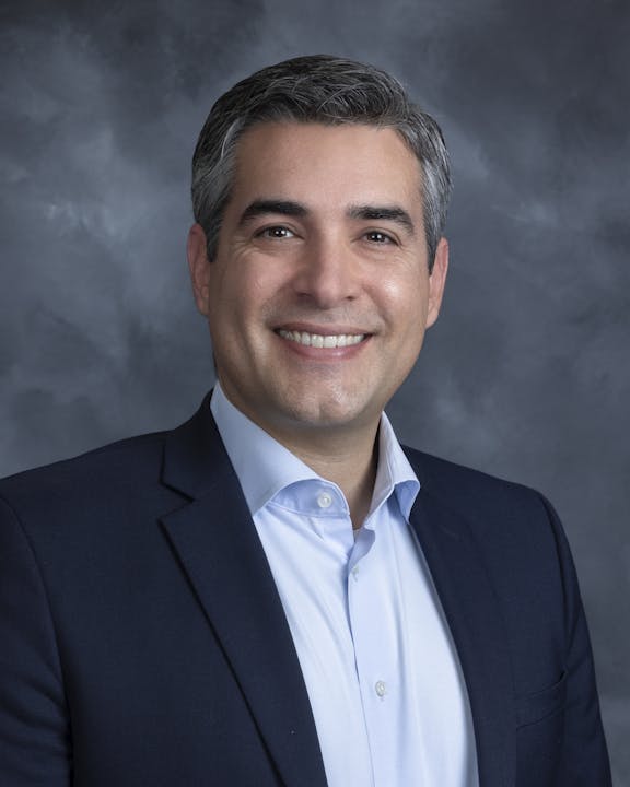Board Member Jonathan Ahmadi portrait in a dark blue suit smiling against a neutral background.