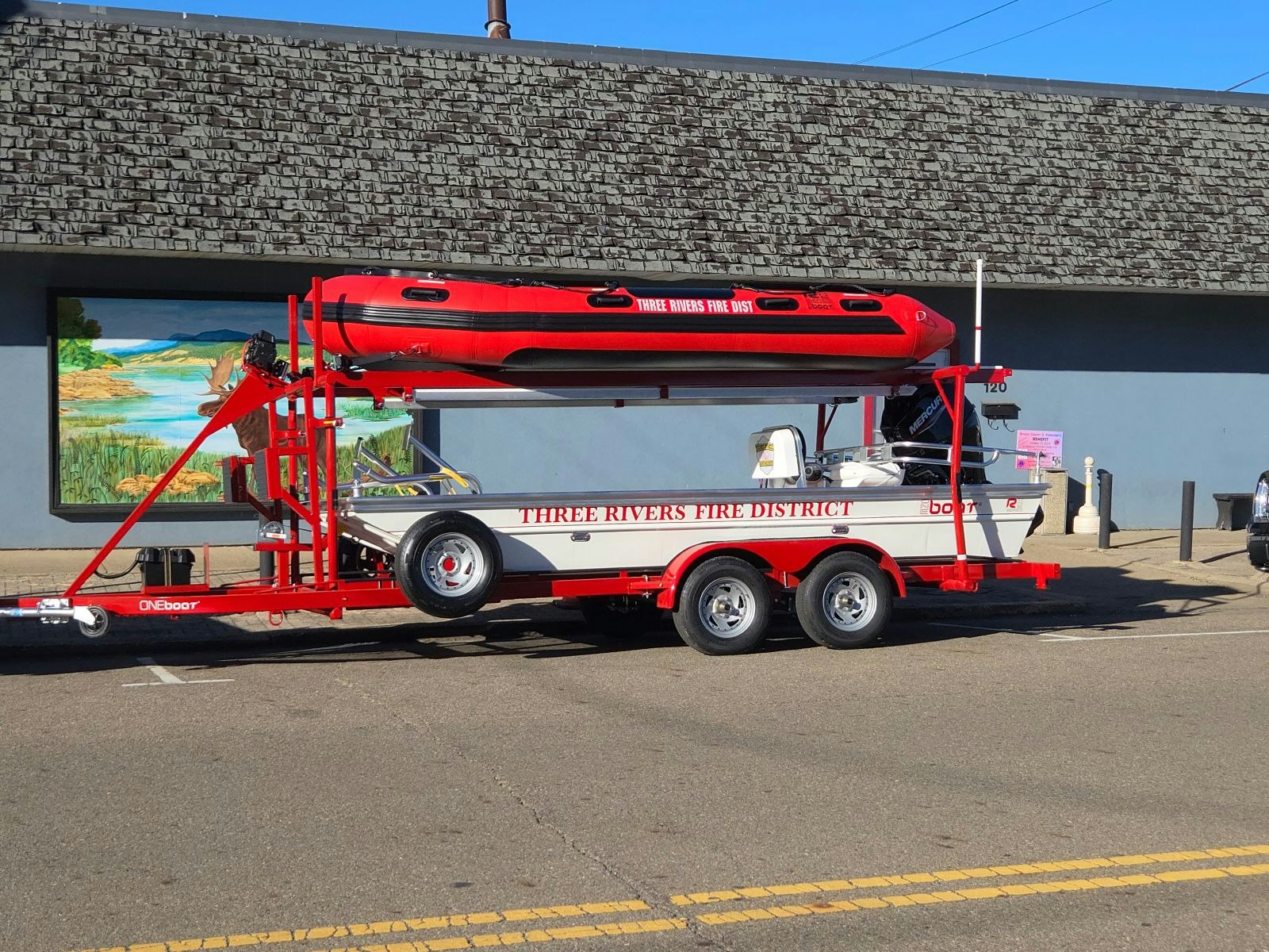 A red fire and rescue boat on a trailer marked "THREE RIVERS FIRE DISTRICT" parked on the street.