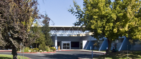 A modern building with a large entrance, surrounded by trees under a clear blue sky.