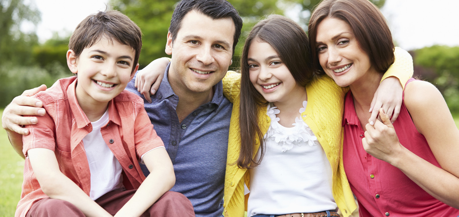 A happy family of four smiling outdoors.