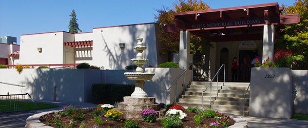 A building entrance labeled "Bloss Memorial Building" with a fountain, flowers, and people by the door.
