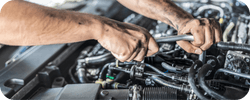 Hands using a wrench on a car engine.