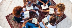 A group of people sitting on a rug, reading books together, showcasing a collaborative and social reading atmosphere.