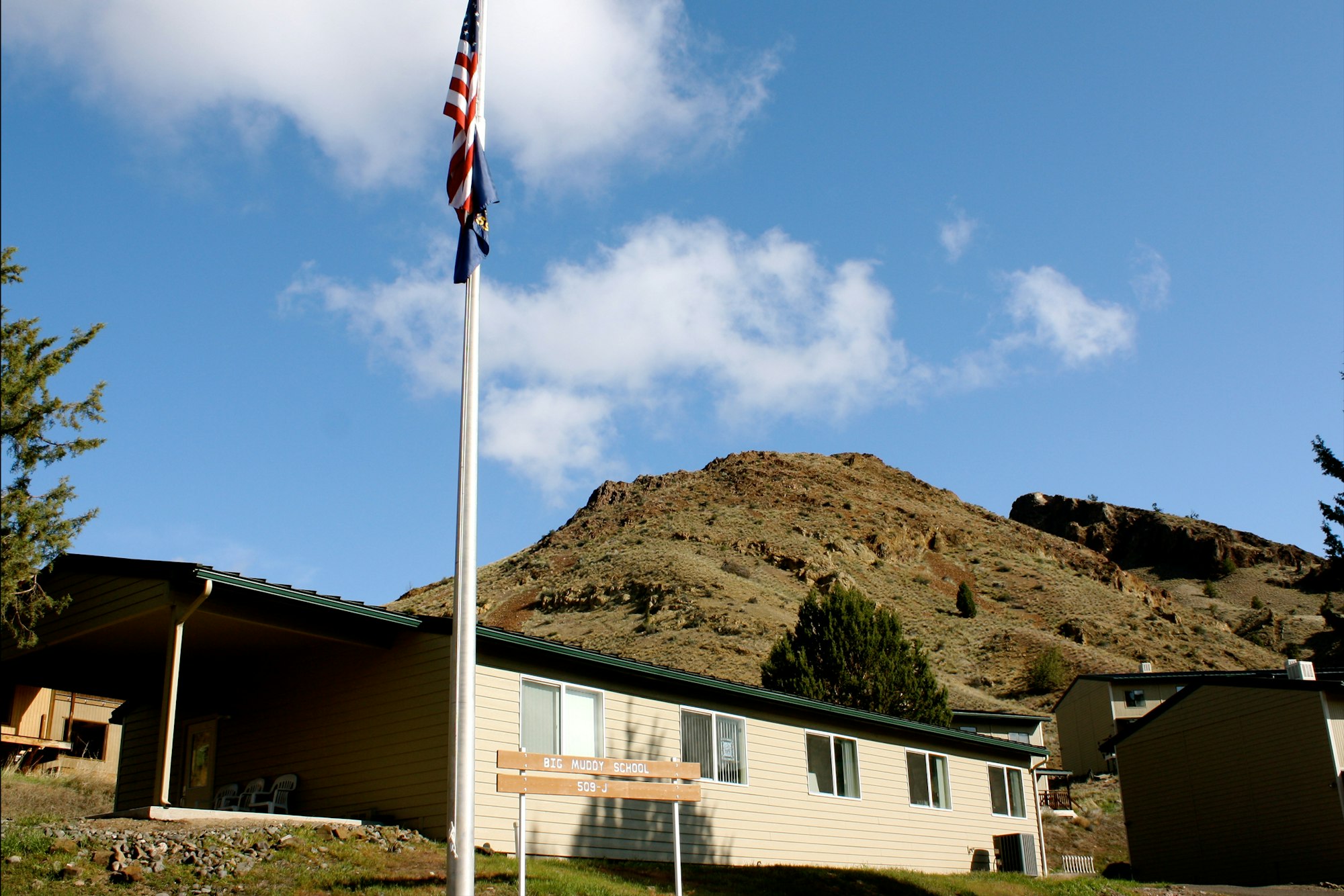 Big Muddy School, Oregon, the school building with flagpole in front of a hill, under a blue sky with clouds.
