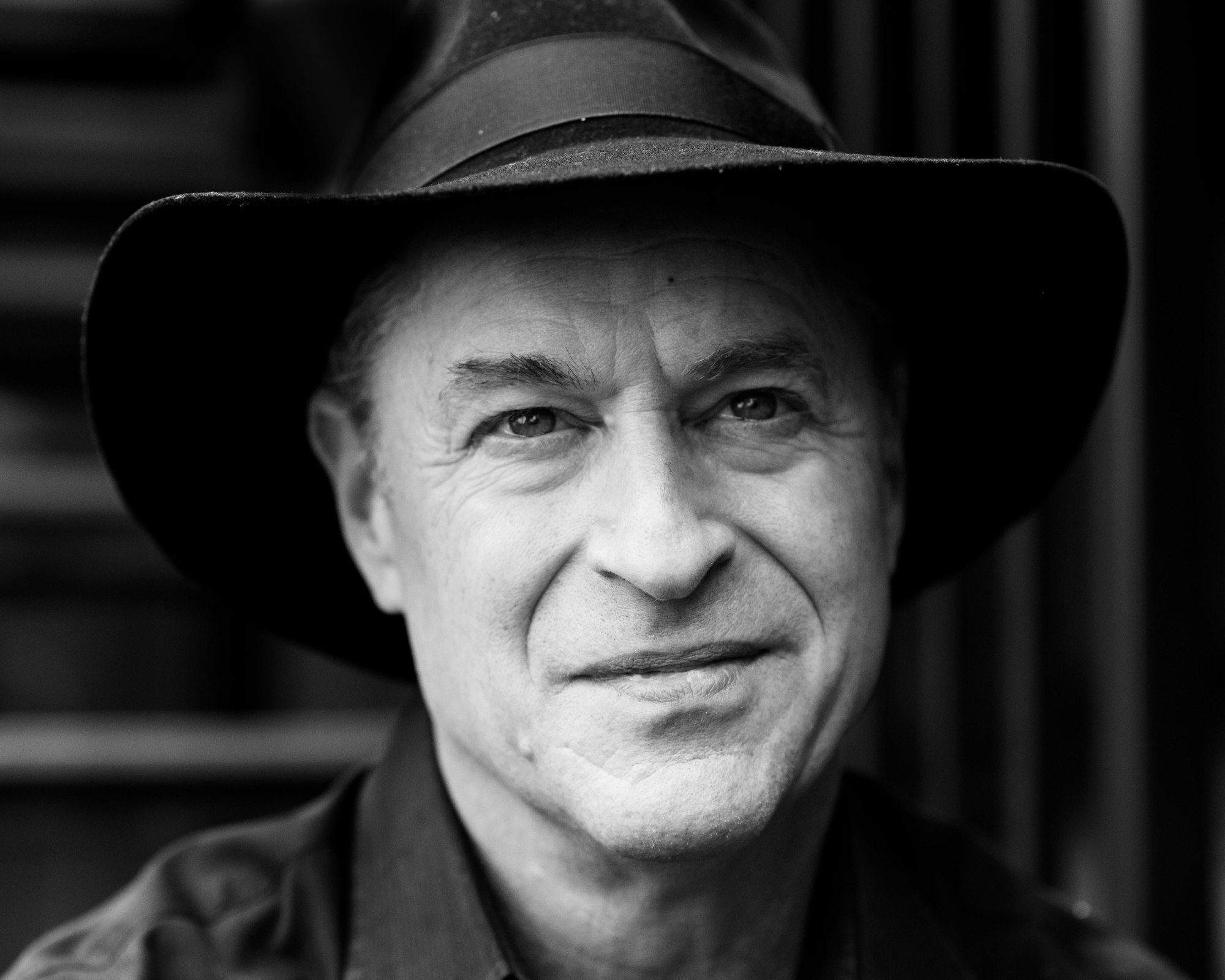 A black and white portrait of a person wearing a hat, smiling slightly.