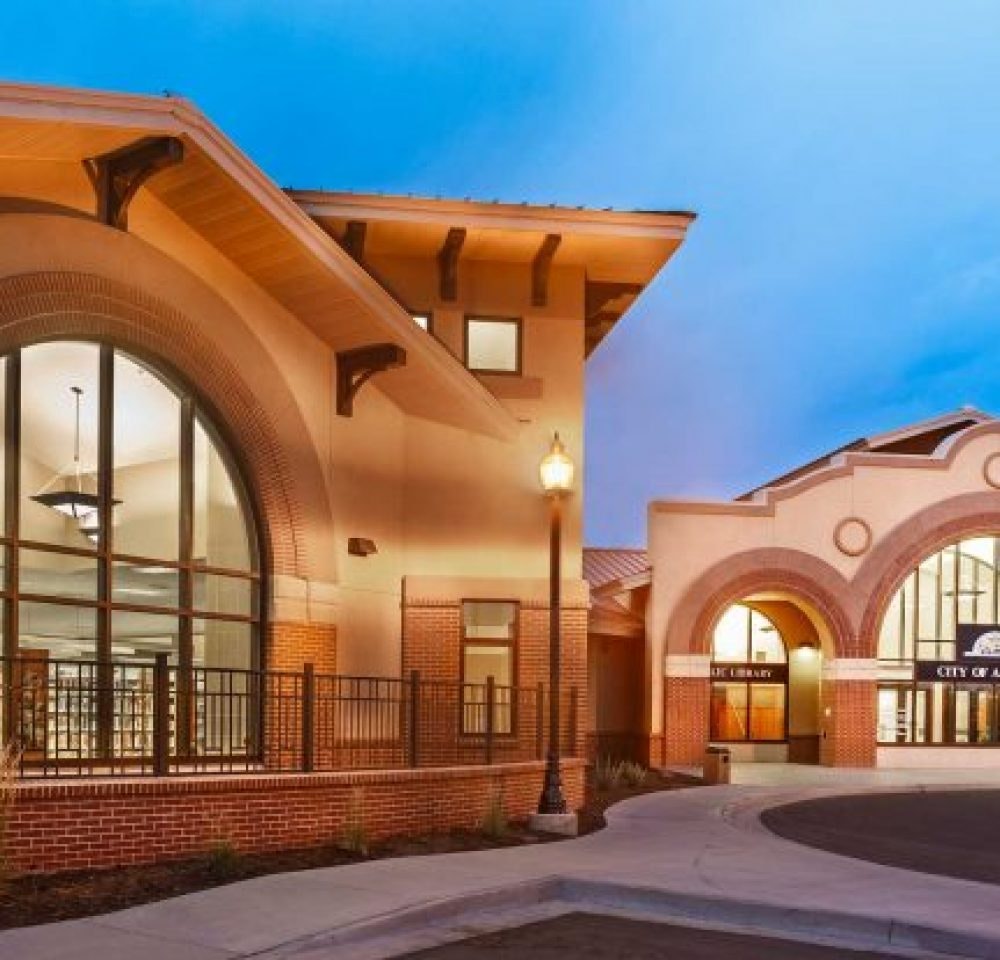 A modern building with arched windows and brick accents, likely a library, is illuminated against a twilight sky.
