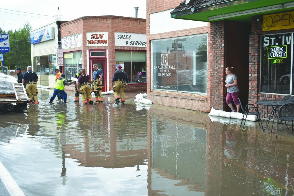 Flooded street scene with people, sandbags, and businesses.