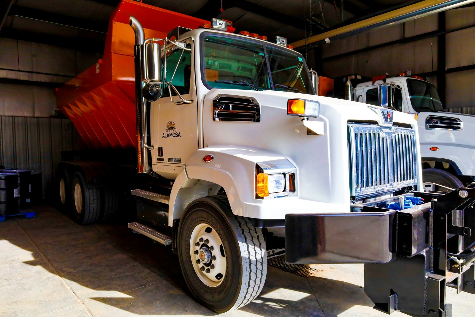 A white dump truck with an orange bed parked inside a garage.