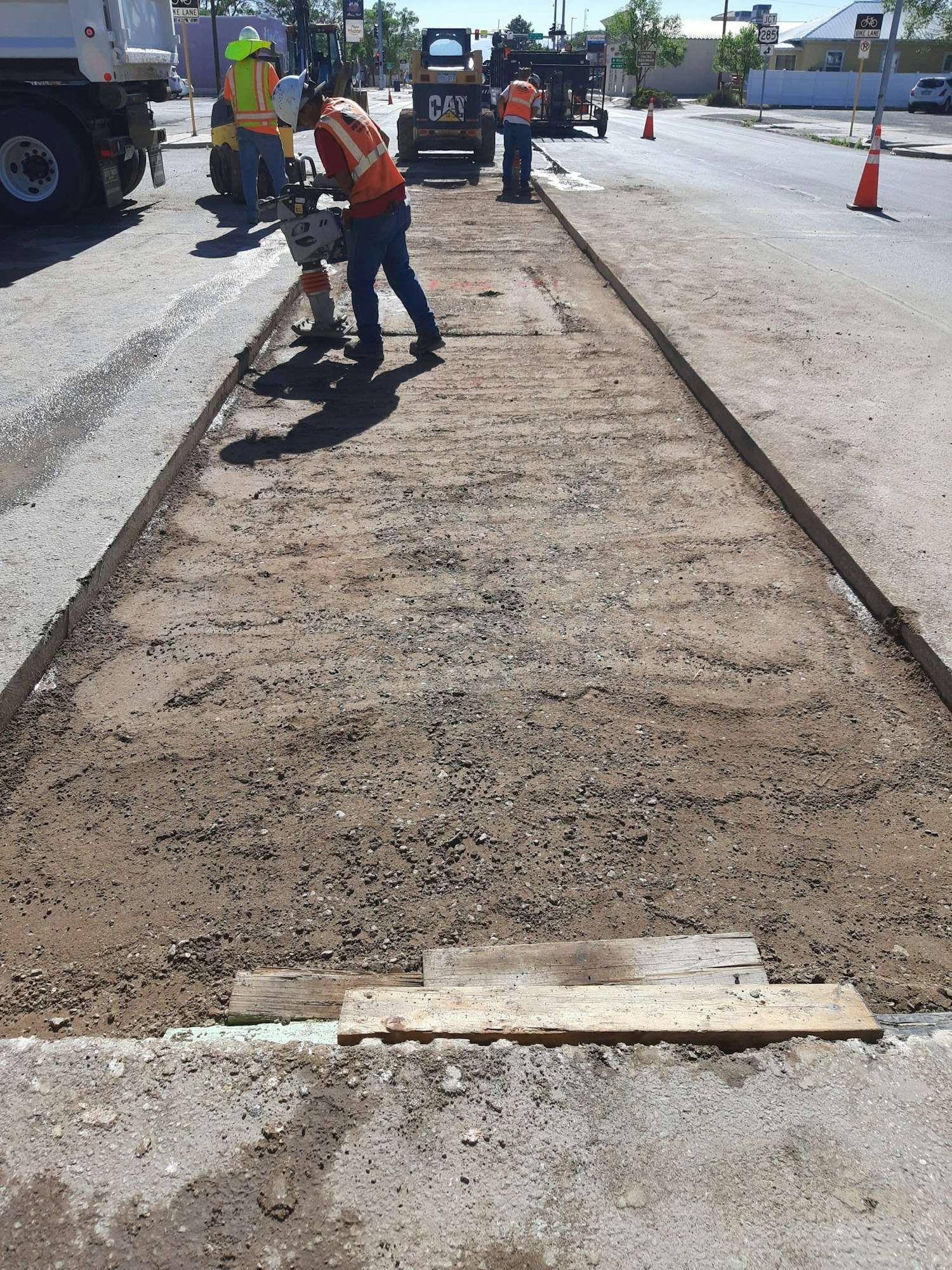 Construction workers repairing a road with machinery and tools, surrounded by traffic cones.