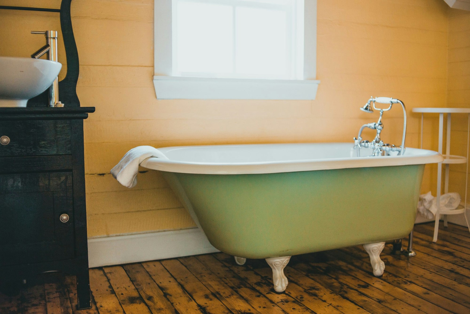 A vintage bathtub with claw feet, a towel draped over the side, and a sink beside it in a rustic bathroom.