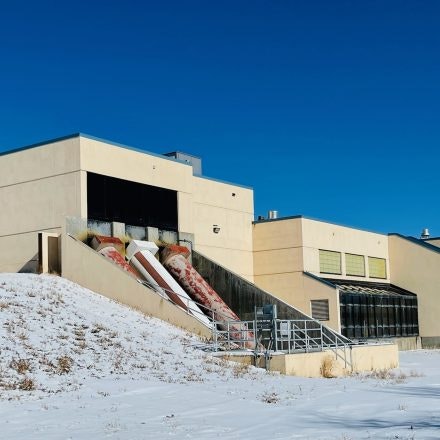 A modern building with large pipes on a snowy hill under a clear blue sky.