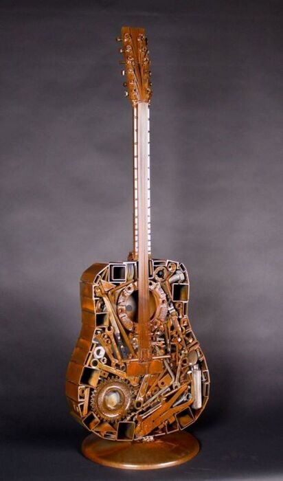 A guitar sculpture made from various mechanical parts and gears, displayed on a stand.