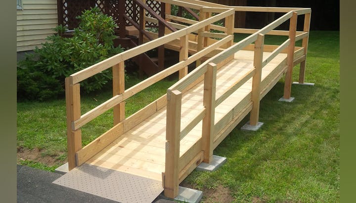 Wooden accessibility ramp leading to a porch, surrounded by grass.