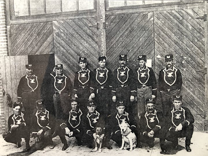A group of uniformed men poses with two dogs in front of a wooden door.