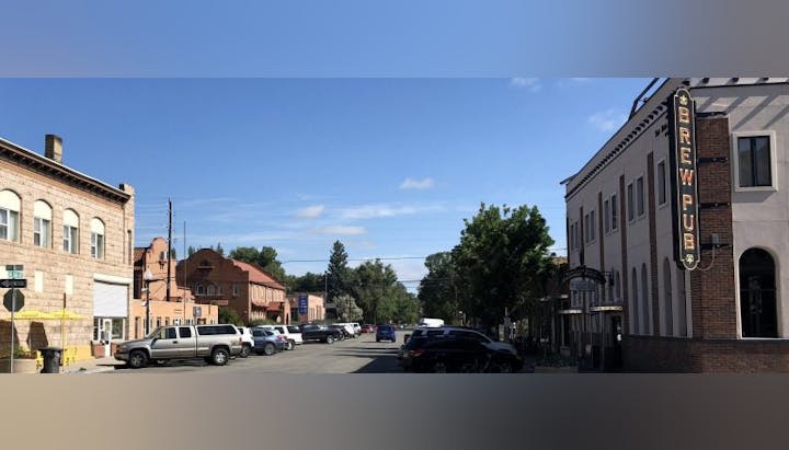 Street scene with parked cars, buildings, a "Brew Pub" sign, and trees under a clear blue sky.