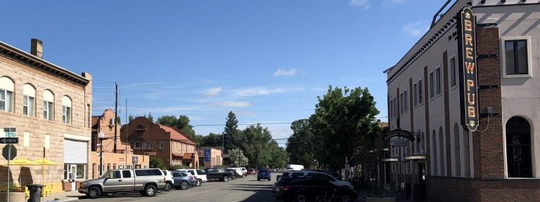 Street scene with parked cars, buildings, a "Brew Pub" sign, and trees under a clear blue sky.
