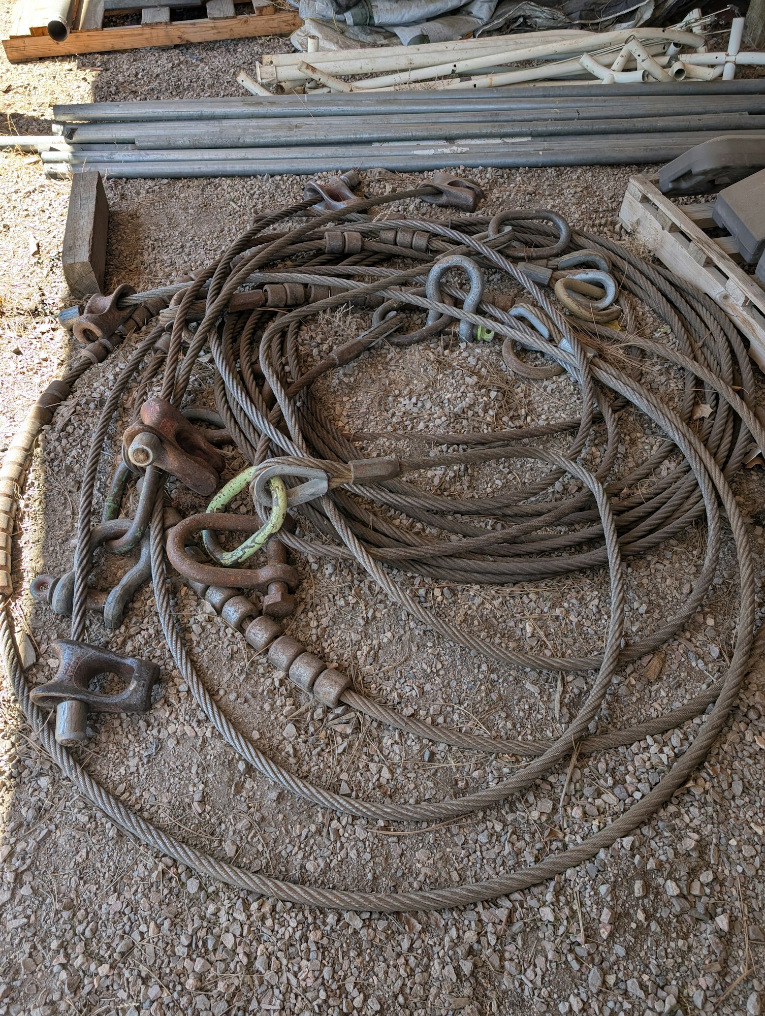 The image shows a tangled arrangement of thick wire cables and various hooks, laid on a gravel surface.