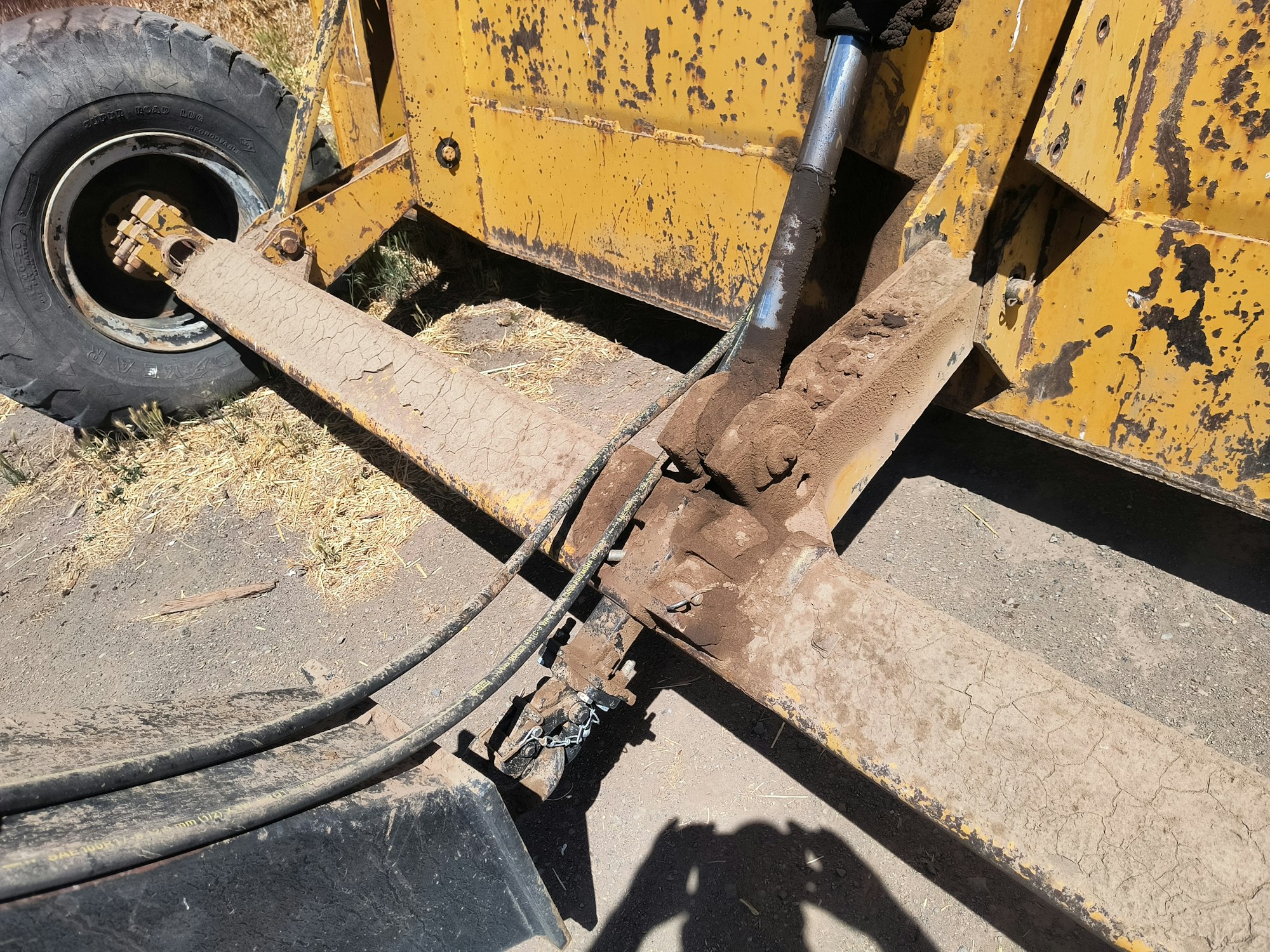 The image shows a close-up of heavy machinery parts, including a rusty hydraulic system and worn-out tires on rough terrain.