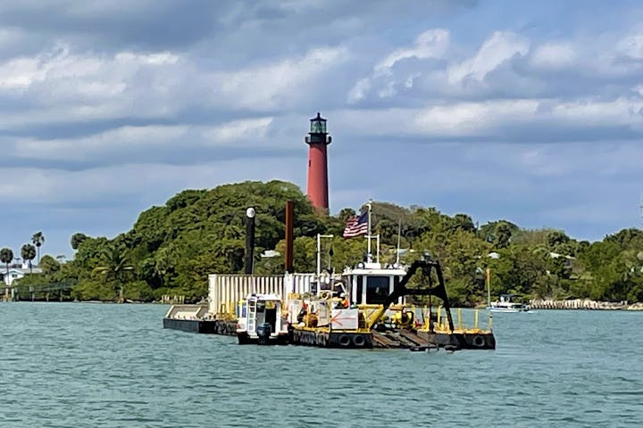 dredge boat floating on water with Jupiter lighthouse in background