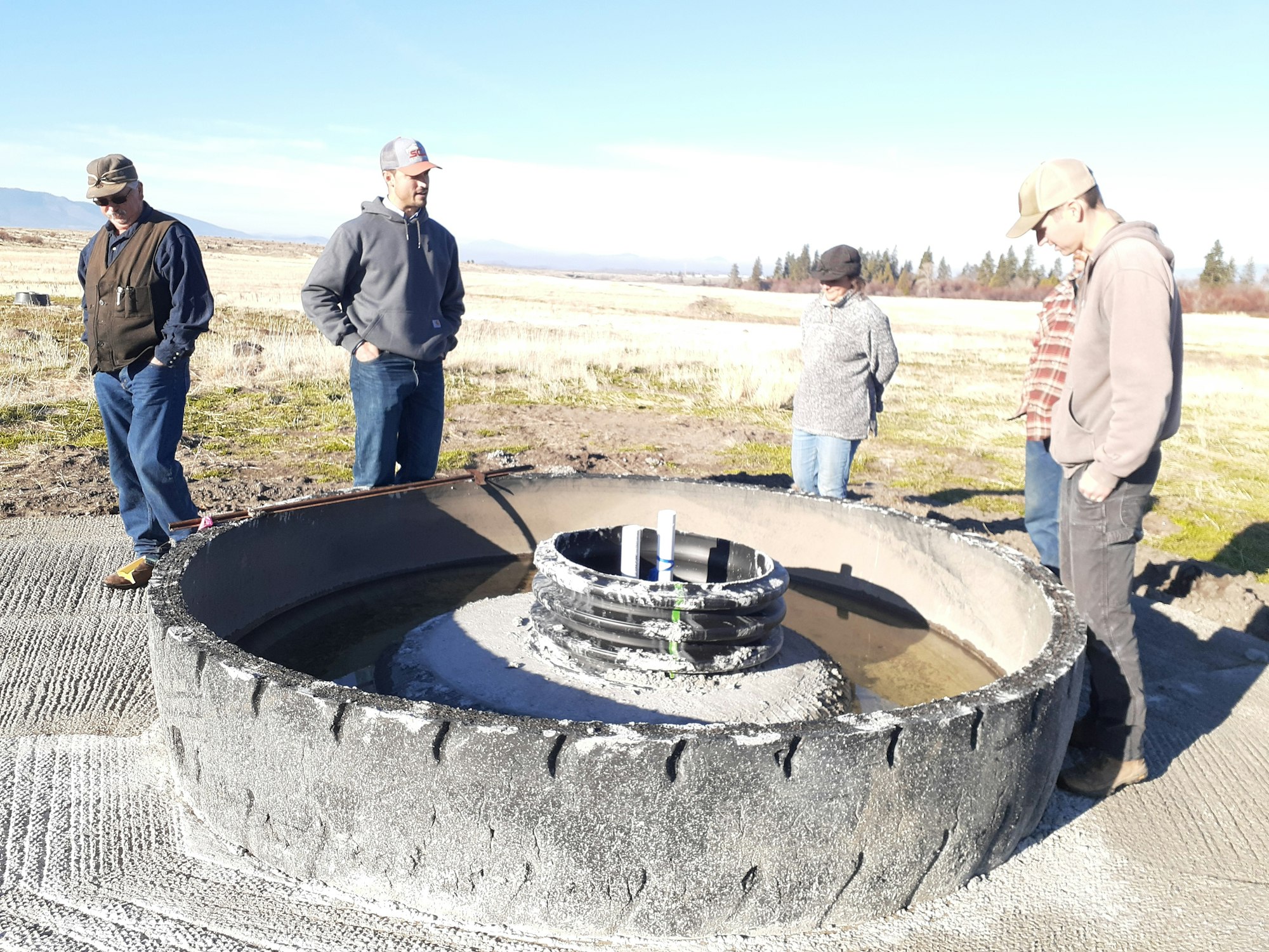 Four people observing an open industrial hatch in an outdoor setting.