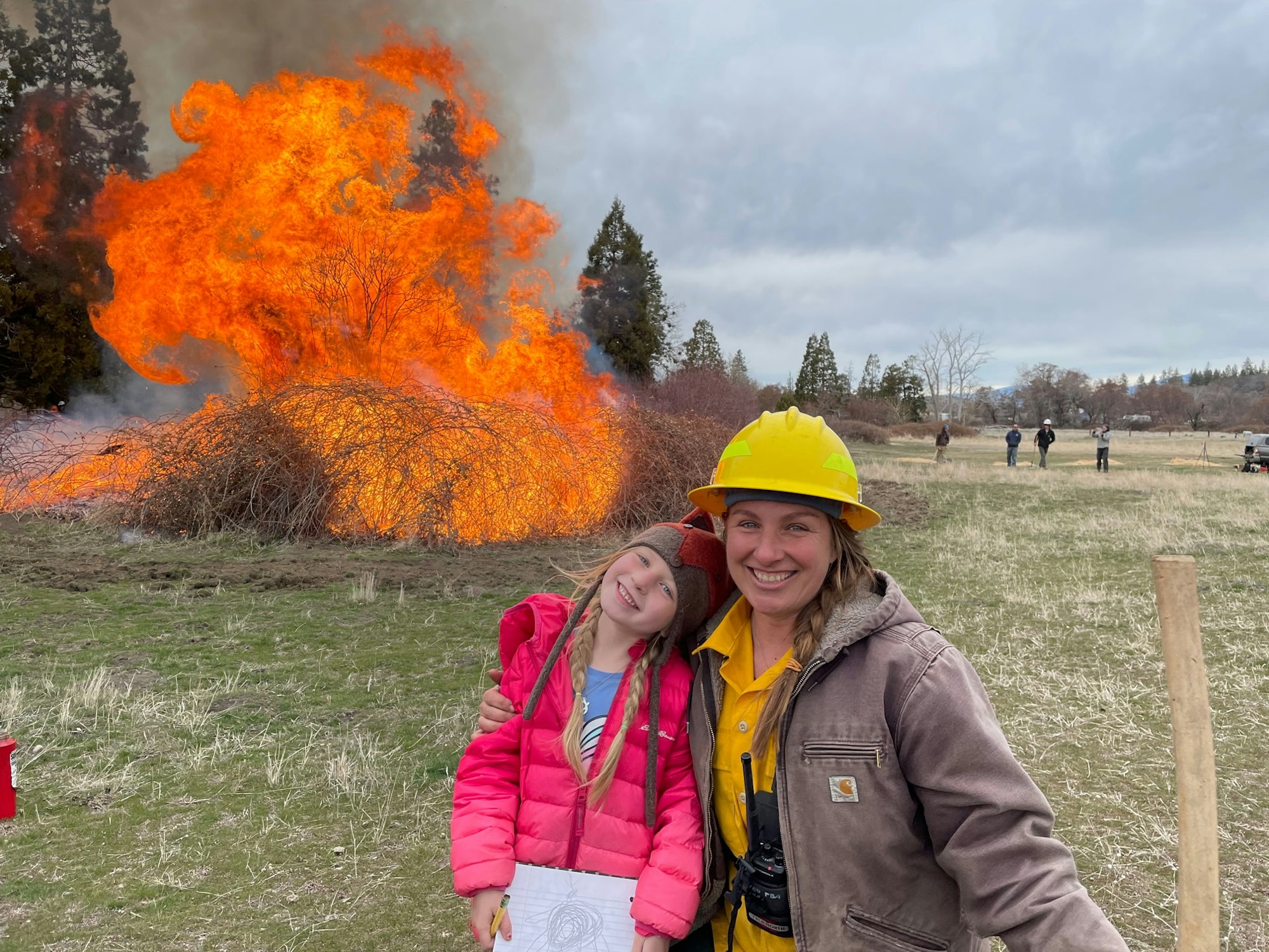 A mother and daughter smiling in front of blackberries on fire in a pasture