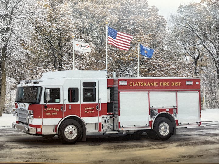 The image shows a red fire truck labeled "Clatskanie Fire Dist." parked in a snowy landscape with trees in the background.