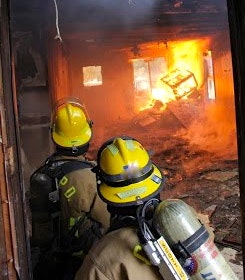 Firefighters facing a blazing inferno inside a building.