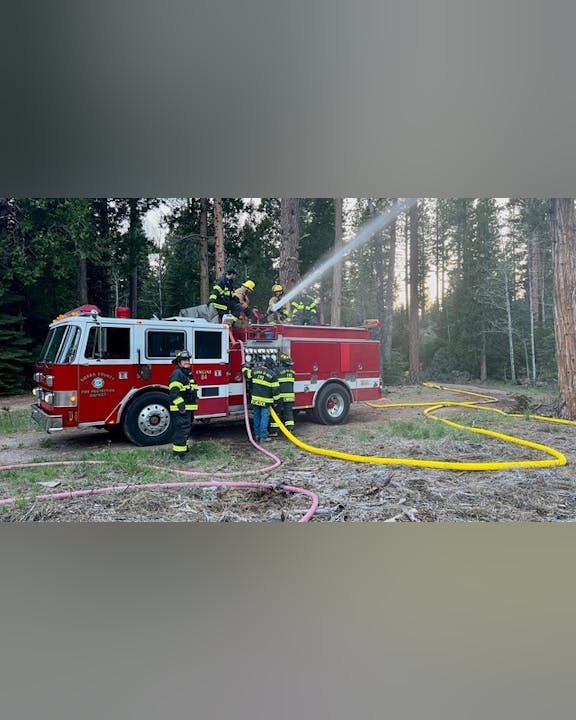 Firefighters operating a fire engine, spraying water in a forested area.