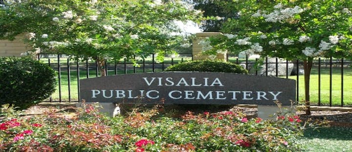 Sign reading "Visalia Public Cemetery" surrounded by flowering bushes and trees.