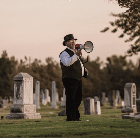 Man with a megaphone in a cemetery at dusk.
