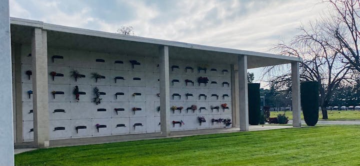 A columbarium wall with niches adorned with flowers at a cemetery.